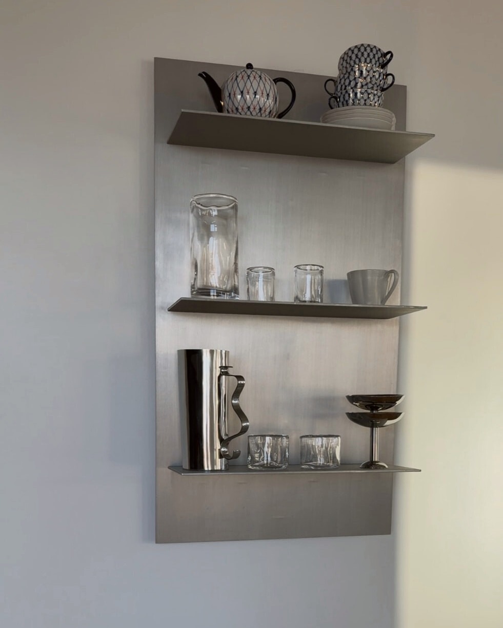 Steel wall shelf with glassware above two wooden stools